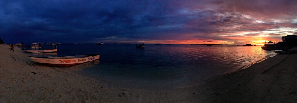 Sunset over Bounty Beach, Malapascua Island, with a Thresher Shark Divers boat on the sand